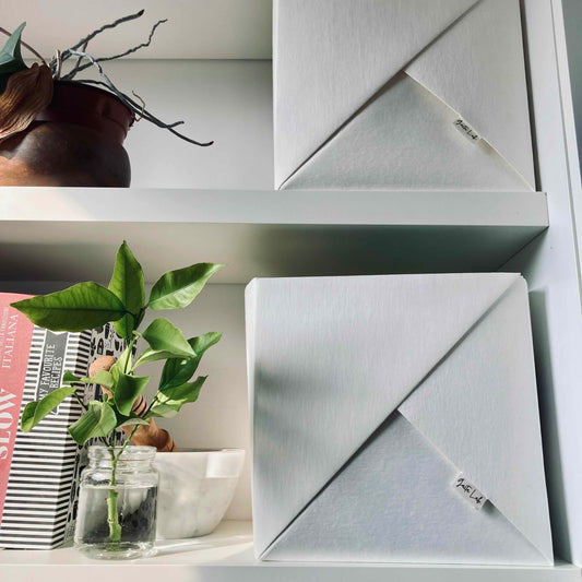 Two origami handmade basket in washable paper warm white with a brand logo on a kitchen shelf with decorative items - Gaita Lab